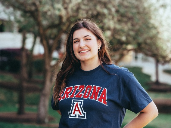 woman wearing blue university of arizona shirt standing in front of trees