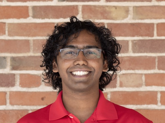 headshot of person wearing red shirt with brick background